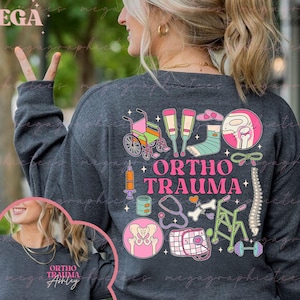 Könnte beinhalten: Ein dunkelgraues Langarmshirt mit einem bunten Grafikdesign, das medizinische Geräte und den Text "Ortho Trauma" zeigt. Die Grafik enthält einen Rollstuhl, Krücken, einen Gips, ein Stethoskop, einen Knochen, einen Rollator und Hanteln. Das Shirt ist anpassbar.