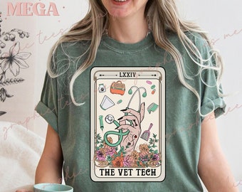 Puede incluir: Una camiseta verde con un diseño de carta de tarot que muestra una mano sosteniendo un estetoscopio y rodeada de flores. La carta dice "LXXIV" y "THE VET TECH".