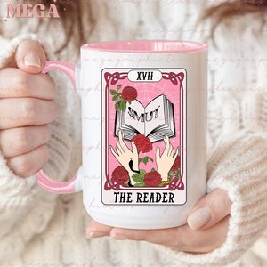 May include: White ceramic mug with a pink rim and handle. The mug features a pink and white tarot card design with the number XVIII and the words "The Reader" and "SMUTI" on the card.
