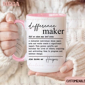 May include: White ceramic mug with a pink rim, featuring the text "difference maker" with a definition and the name "Harper" written below. The mug is held by a hand wearing a white sweater. The text "CUSTOMIZABLE" is visible at the bottom of the image.