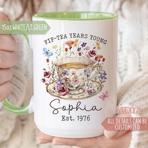 May include: White ceramic mug with a light green interior and handle. The mug features a floral teacup design with the text "FIF-TEA YEARS YOUNG", "Sophia", and "Est. 1976". The mug holds 15oz.