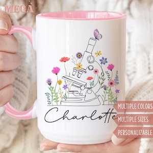 May include: White ceramic mug with a pink interior and handle. The mug features a black line drawing of a microscope surrounded by colorful flowers and a butterfly. The name "Charlotte" is written in script.
