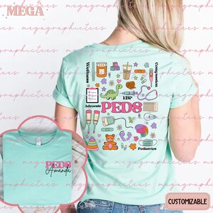 K&ouml;nnte beinhalten: Ein hellblaues T-Shirt mit einem bunten Grafikdesign, das das Wort "PEDS" zeigt, umgeben von verschiedenen medizinischen Symbolen und Illustrationen. Der Text "PEDS Amanda" ist auch auf der Vorderseite des Shirts zu sehen.