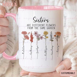 Op de afbeelding: Een witte keramische mok met een roze rand en handvat. De mok heeft een bloemenmotief met de tekst "Sisters are different flowers from the same garden". De namen Natalie, Anthony, Jardyn, Kathlynn, Lourtney en Henry staan onder de bloemen.