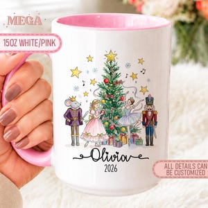 Può includere: Una tazza in ceramica bianca da 444 ml con interno e manico rosa. L'esterno presenta un'illustrazione di un albero di Natale con un topo con corona, una ragazza in abito rosa, una ballerina e uno schiaccianoci. Il testo riporta Olivia 2026.