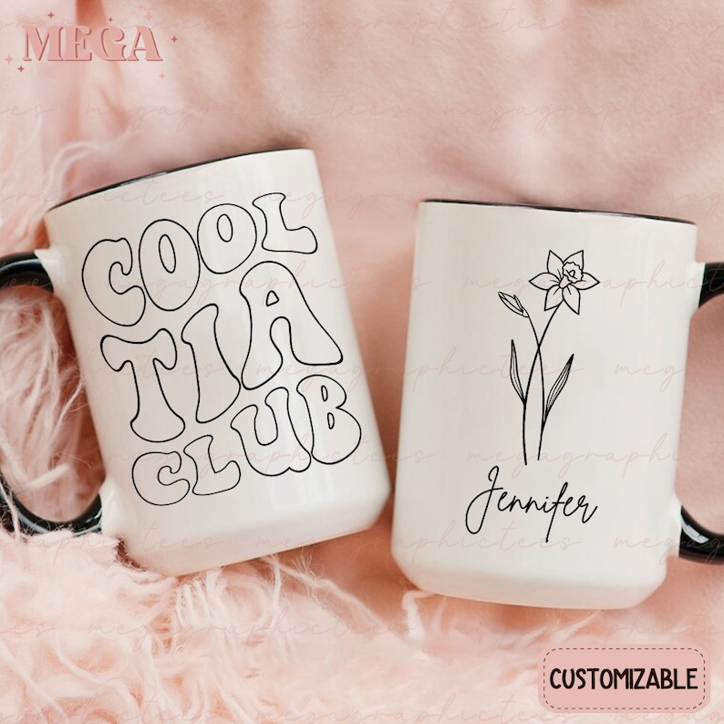 May include: Two white ceramic mugs with black handles. One mug has the text "Cool Tia Club" in black outlined letters. The other mug has a black line drawing of a flower and the name "Jennifer" written in cursive.