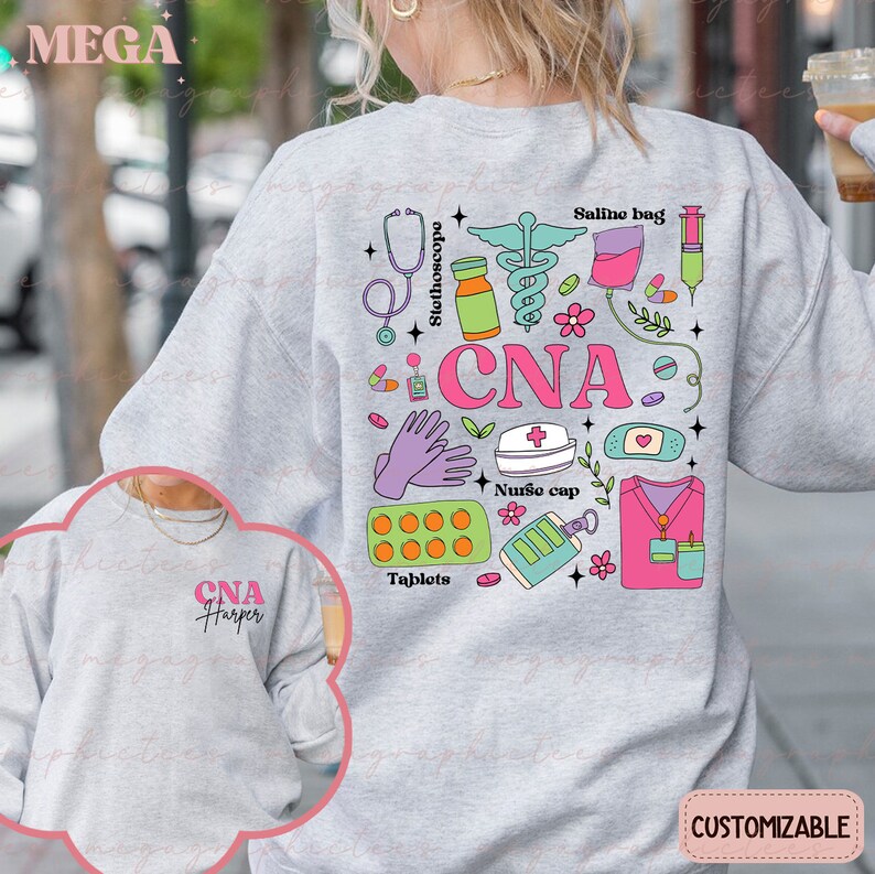 Op de afbeelding: Een grijs sweatshirt met een roze, blauw en groen ontwerp van medische instrumenten en de tekst "CNA". Het sweatshirt heeft een kleiner ontwerp op de linkermouw met de tekst "CNA Harper".