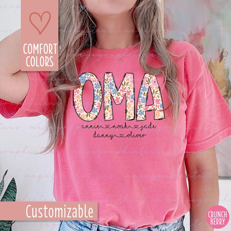 Puede incluir: Una camiseta rosa con la palabra "OMA" en un dise&ntilde;o floral. Debajo, los nombres "annie", "noah", "jade", "danny" y "oliver" est&aacute;n impresos. La camiseta tambi&eacute;n tiene las palabras "Comfort Colors" y "Customizable".