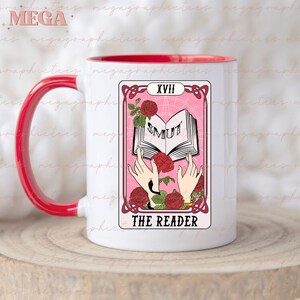 May include: White ceramic mug with a red rim and handle. The mug features a pink tarot card design with the number XVIII and the words "THE READER" and "SMUT" on the card.