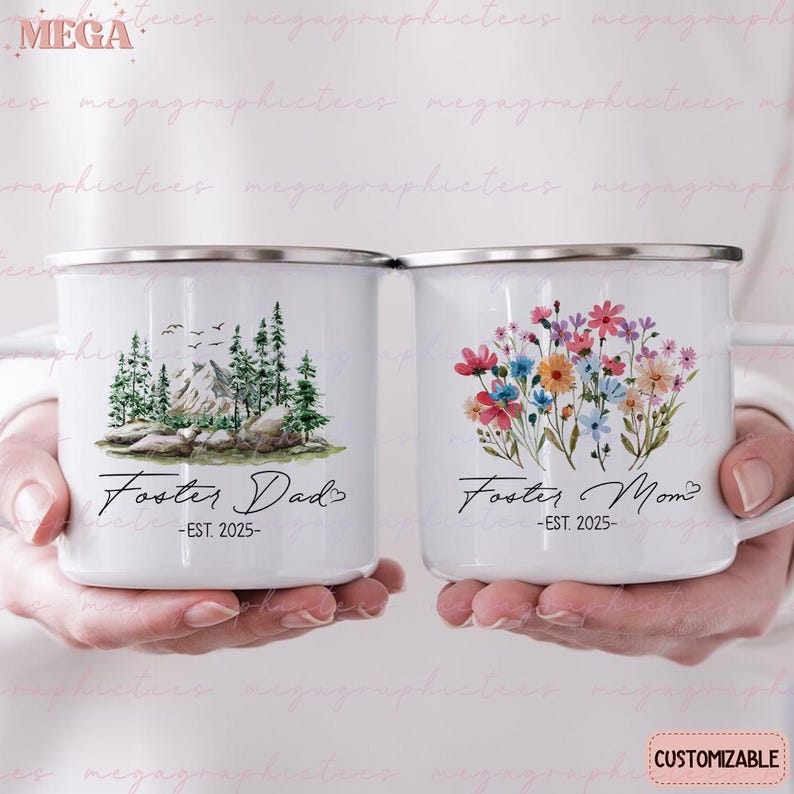 K&ouml;nnte beinhalten: Zwei wei&szlig;e Emailletassen mit schwarzem Text und Bildern. Die Tasse links zeigt eine Berglandschaft mit B&auml;umen und dem Text "Foster Dad - EST. 2025". Die Tasse rechts zeigt einen Strau&szlig; bunter Blumen und den Text "Foster Mom - EST. 2025".