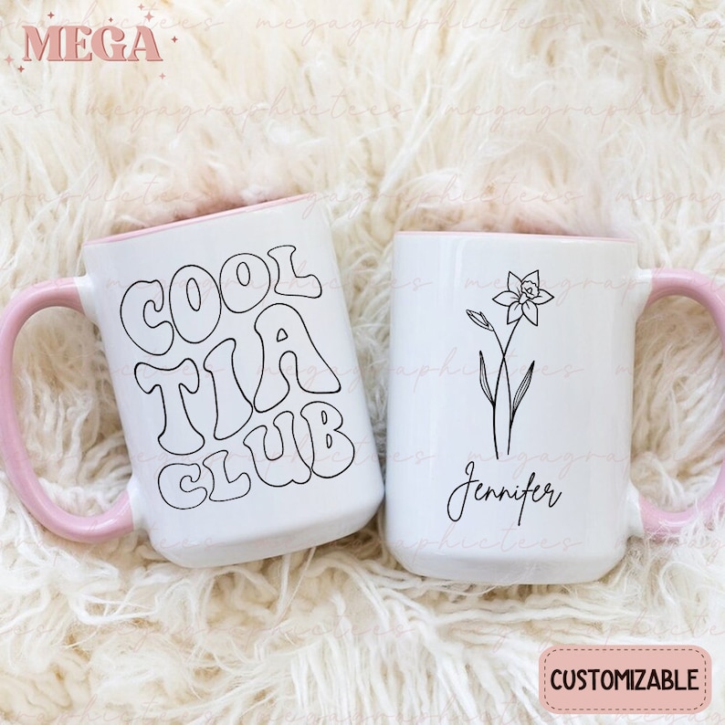 May include: Two white ceramic mugs with pink rims. One mug has the text "Cool Tia Club" in black outlined letters. The other mug has a black line drawing of a flower and the text "Jennifer".
