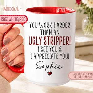 Op de afbeelding: Een witte keramische mok met een rode binnenkant en handvat, voorzien van de zwarte en rode tekst: YOU WORK HARDER THAN AN UGLY STRIPPER! I SEE YOU & I APPRECIATE YOU! Sophie met een klein rood hartje onder de naam.