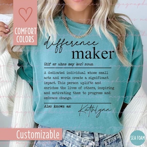 Pode incluir: Uma camiseta azul turquesa com o texto "difference maker" definido como "um indivíduo dedicado cujas pequenas ações e palavras criam um impacto significativo". O texto "Also known as: Kathlynn" está abaixo da definição. A camiseta é personalizável.