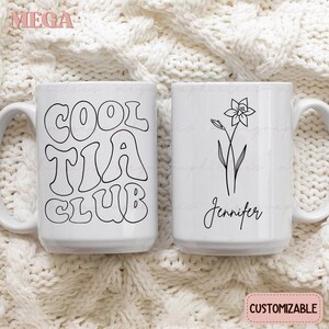 May include: Two white ceramic mugs with black designs. One mug has the text "Cool Tia Club" in a retro font. The other mug has a simple line drawing of a daffodil and the name "Jennifer".