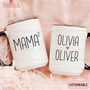 May include: Two white ceramic mugs with black handles. The mug on the left has the text "MAMA^2" in black. The mug on the right has the text "OLIVIA OLIVER" in black with a small pink heart between the names. The mugs are on a pink fuzzy surface. The text "CUSTOMIZABLE" is at the bottom of the image.