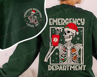 Op de afbeelding: Groene kersttrui met een skelet dat een kerstmanmuts draagt en een koffiemok met een rood kruis vasthoudt. De tekst op de trui is "Emergency Department".