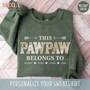 May include: Military green sweatshirt with the text "THIS PAWPAW BELONGS TO" and personalized names below. The word "PAWPAW" is designed with a map-like pattern. The sweatshirt is a comfortable, casual style.