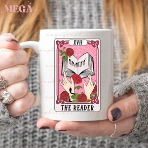 May include: White ceramic mug with a pink and white tarot card design. The card is labeled "XVIII The Reader" and features a book with the word "SMUT" on the cover.
