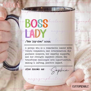 May include: White ceramic mug with a black rim and handle. The mug has a colorful graphic that says "Boss Lady" with a definition below. The definition reads: "A person who is a remarkable leader with vision, compassion, and determination. Her guidance inspires, her empathy supports, and her strength empowers others. She transforms challenges into opportunities, making a lasting, positive impact." The text "Also known as" is followed by the name "Sophia". The mug is customizable.