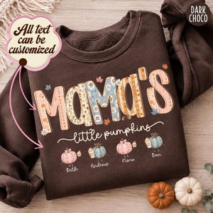 Könnte beinhalten: Ein dunkel schokoladenbraunes Sweatshirt mit Rundhalsausschnitt und dem Text MAMA'S little pumpkins in einem Blumen- und Kürbismuster. Unter dem Text befinden sich vier illustrierte Kürbisse mit Gesichtern, beschriftet mit Beth, Andrew, Nora und Ben.