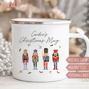 May include: White enamel mug with a silver rim and handle. The mug features the text "Cadie's Christmas Mug" in script, along with illustrations of four colorful nutcracker soldiers. The mug also has text that says "MULTIPLE COLORS", "MULTIPLE SIZES", and "PERSONALIZABLE".