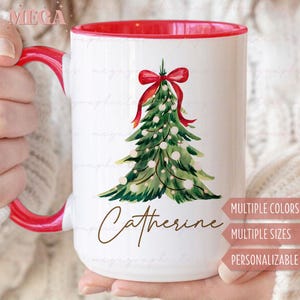May include: White ceramic mug with a red interior and handle. The mug features a watercolor Christmas tree design with a red bow and the name "Catherine" in a script font. Text on the side indicates multiple colors, sizes, and personalization options.