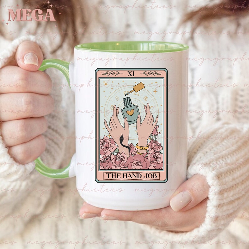 May include: A white ceramic mug with a green rim features a tarot card design. The card depicts a pair of hands holding a bottle of nail polish with a heart on the label. The card is titled "The Hand Job" and has the Roman numeral "XI" in the top corner.