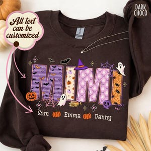 Könnte beinhalten: Ein dunkel schokoladenbraunes Sweatshirt mit Rundhalsausschnitt und dem Wort MIMI in großen Blockbuchstaben, verziert mit Halloween-Mustern wie Fledermäusen, Geistern, Kürbissen und Spinnen sowie den Namen Sam, Emma und Danny im unteren Bereich.