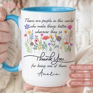 May include: White ceramic mug with a blue interior and handle. The mug features a floral design with the text "There are people in this world who make things better wherever they go. Thank You... for being one of them Amelia."