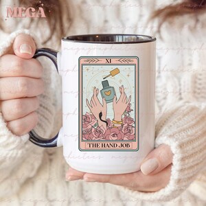 May include: A white ceramic mug with a black rim and handle. The mug features a tarot card design with a light blue background and pink roses. The card depicts two hands holding a bottle of nail polish with a heart on the label. The card is labeled "XI" and "THE HAND JOB".
