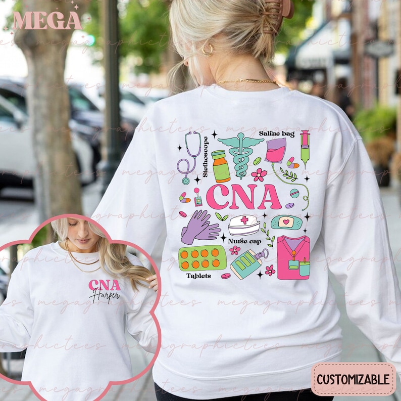 Op de afbeelding: Wit sweatshirt met een roze, groene en blauwe grafische afbeelding van medische instrumenten en de tekst "CNA". De afbeelding bevat een stethoscoop, pillen, een zoutoplossingzak, een verband, een verpleegstersmuts en handschoenen. Het sweatshirt is aanpasbaar.
