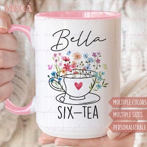 May include: A white ceramic mug with a pink rim features a floral design with a teacup and the text "Bella Six-Tea". The mug is personalised with a name and has a heart-shaped design.