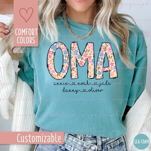 Puede incluir: Camiseta verde agua con la palabra "OMA" en letras florales grandes. Debajo de la palabra "OMA" est&aacute;n los nombres "annie", "noah", "jade", "danny" y "oliver". Tambi&eacute;n son visibles las palabras "Comfort Colors" y "Customizable".