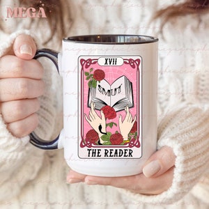 May include: White ceramic mug with a black handle. The mug features a pink and black tarot card design with the text "THE READER" and "SMUT" on the card. The card number is "XVIII".