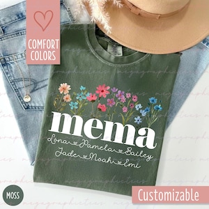 Può includere: T-shirt verde muschio con la parola "mema" in bianco, nomi sotto e un disegno floreale sopra. Personalizzabile, realizzata con colori confortevoli. Il testo "Comfort Colors" è visibile.