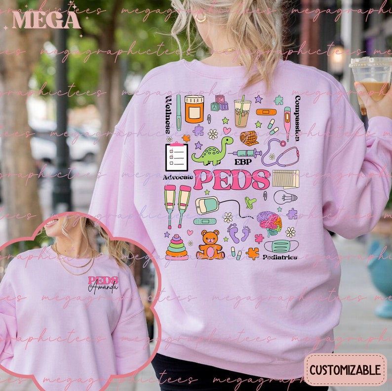 K&ouml;nnte beinhalten: Rosafarbener Pullover mit einem bunten Grafikdesign aus medizinischen Symbolen und dem Wort "PEDS" in der Mitte. Die Grafik enth&auml;lt ein Stethoskop, ein Thermometer, eine Spritze, einen Verband, einen Teddyb&auml;r, einen Dinosaurier und andere medizinische Symbole. Der Text "Advocate", "EBP", "Wellness", "Compassion" und "Pediatrics" ist ebenfalls in der Grafik enthalten.