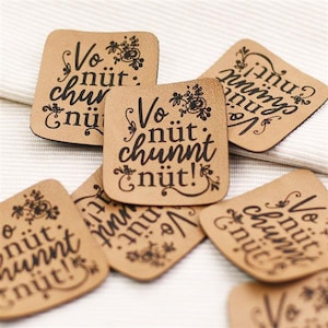 Könnte beinhalten: Sechs braune Lederpatches mit schwarzer Beschriftung. Die Patches zeigen den Spruch "Vo nüt chunnt nüt!" was im Deutschen "Nichts kommt umsonst!" bedeutet. Die Patches sind perfekt, um Ihren Bastelarbeiten einen rustikalen Charme zu verleihen.