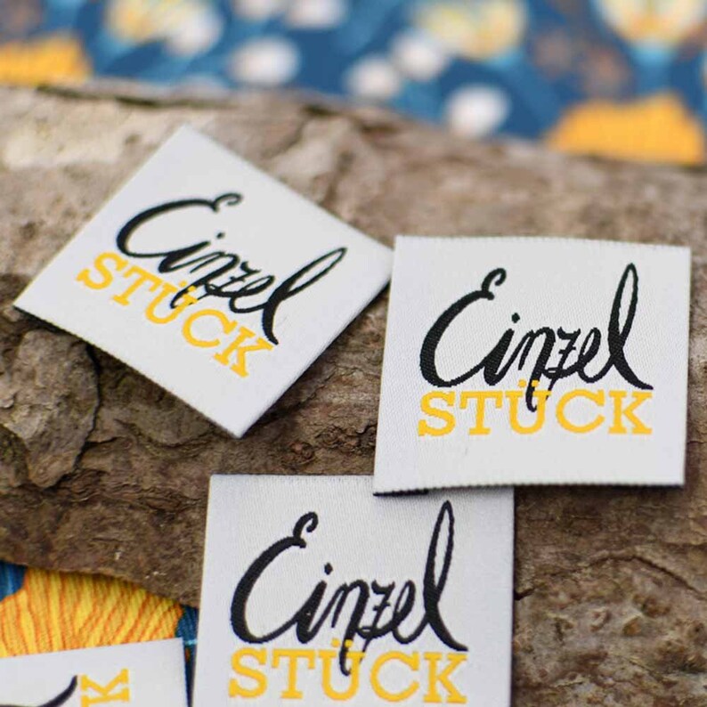 May include: Three white fabric labels with black and yellow text that reads "Einzel Stuck".