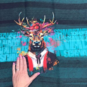 Könnte beinhalten: Ein farbenfrohes Grafikdesign eines Hirsches mit Hut, Anzug und Hosenträgern. Der Hirsch ist vor einem türkis-dunkelgrünen gestreiften Hintergrund mit dem Wort "SCHWARZWALD" in Türkis platziert. Farbspritzer in Pink, Orange und Blau umgeben den Hirsch.