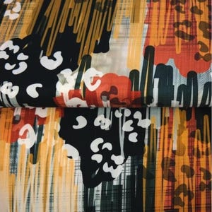 Könnte beinhalten: Abstraktes Stoffmuster mit kräftigem Design. Das Muster zeigt schwarze, weiße, orangefarbene und goldfarbene Pinselstriche und Formen. Der Stoff hat ein geschichtetes Aussehen, wobei die obere Schicht leicht über der unteren gefaltet ist.