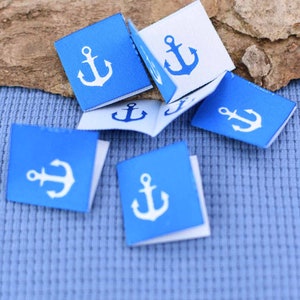 Peut inclure: Plusieurs petits carrés de tissu avec un motif d'ancre. Les étiquettes sont principalement bleues avec une ancre blanche, et certaines sont blanches avec une ancre bleue. Elles sont pliées et semblent neuves.