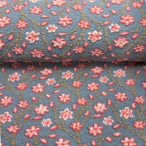 Könnte beinhalten: Eine Rolle blauer Stoff mit einem sich wiederholenden Muster aus rosa Kirschblüten und braunen Zweigen. Der Stoff hat ein strukturiertes, erhabenes Design, das einen dreidimensionalen Effekt erzeugt. Die Blüten sind in voller Blüte.