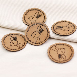 May include: Five brown leather patches with a white stitched border and a black line drawing of a bunny rabbit on each.