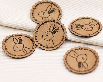 May include: Five brown leather patches with a white stitched border and a black line drawing of a bunny rabbit on each.