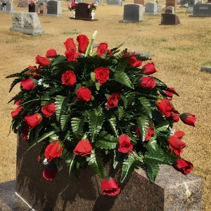 Puede incluir: Un arreglo floral de rosas rojas sobre una lápida de granito. Las rosas están dispuestas en forma circular y están rodeadas de follaje verde.
