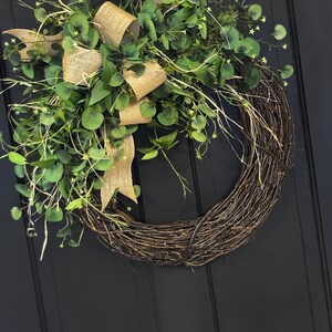 May include: A brown grapevine wreath with a burlap bow and green eucalyptus leaves.