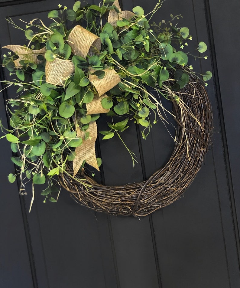 May include: A brown grapevine wreath with a burlap bow and green eucalyptus leaves.