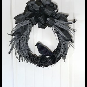 May include: A black raven sits on a black twig wreath with a large black satin bow. The wreath is decorated with gray sprigs.