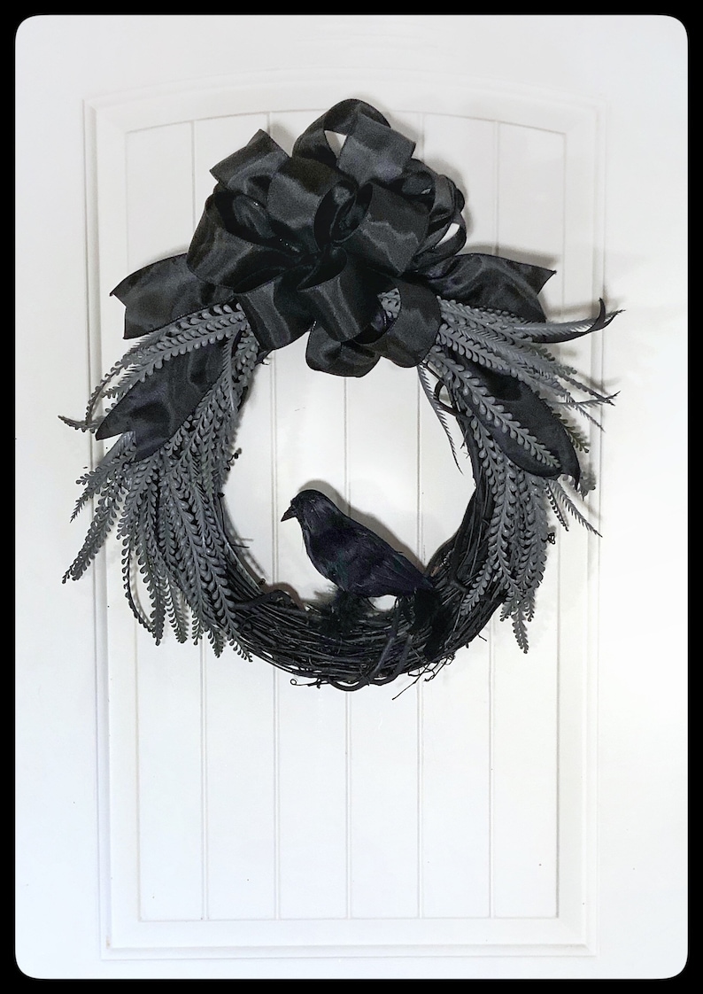 May include: A black raven sits on a black twig wreath with a large black satin bow. The wreath is decorated with gray sprigs.