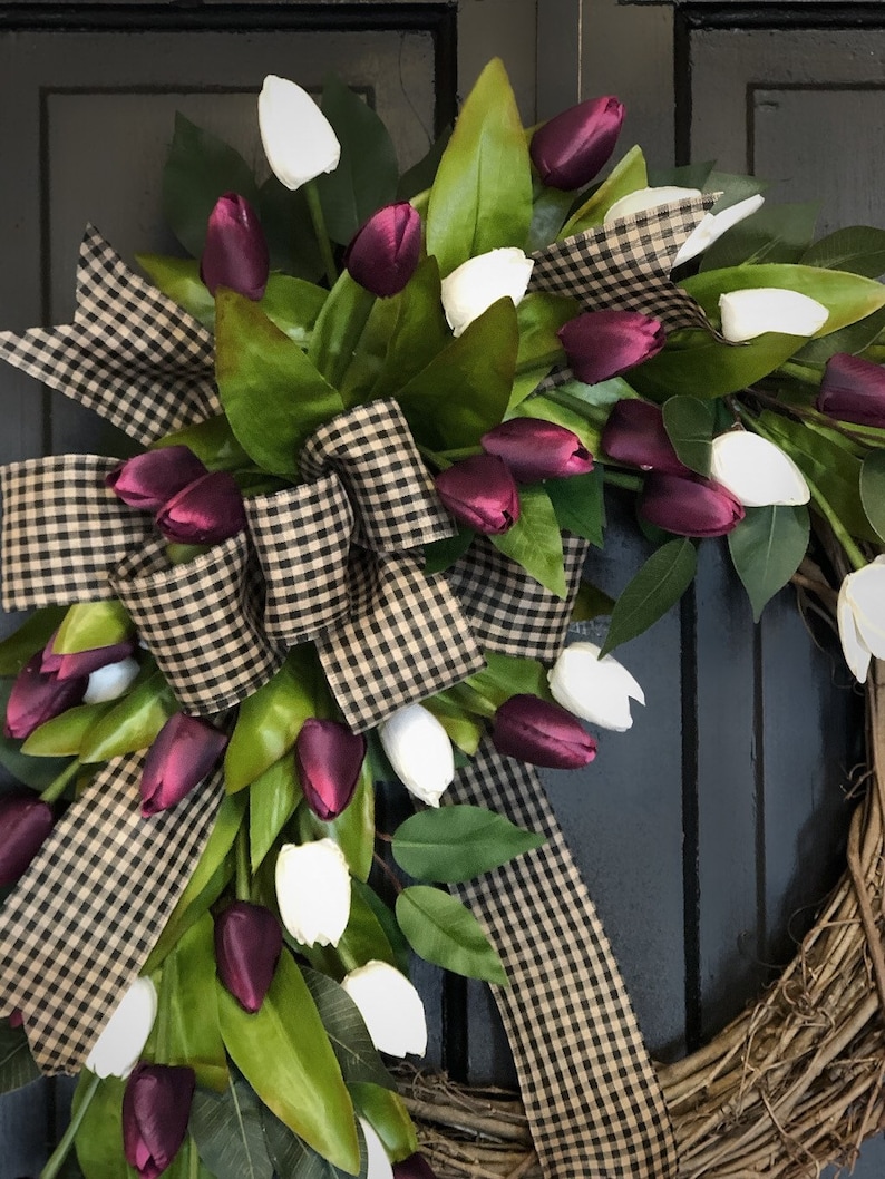 May include: A grapevine wreath with a black and white checkered ribbon bow and a cascade of white and burgundy tulips.